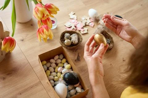 Woman decorating handmade Easter eggs with feathers at home Foto stock