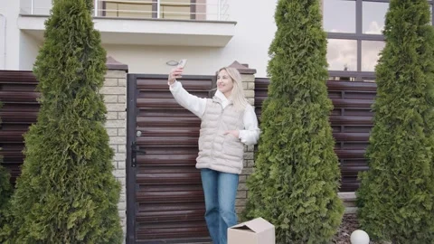 Woman delivering a box while taking a selfie by the entrance of a house Stock Footage 316595331