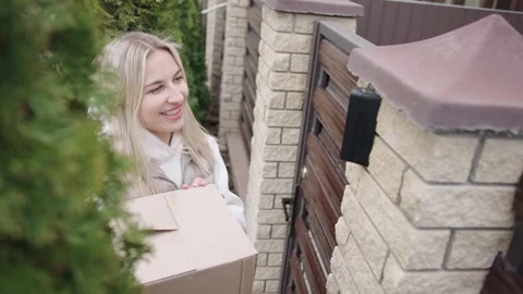 Woman delivers a package at a gate while smiling and waving on a sunny day Video stock 316596337