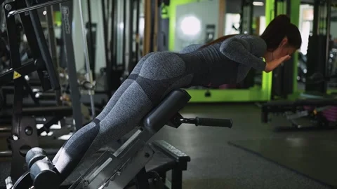 A woman demonstrates a back extension exercise in a gym environment. She is Stock Footage 345025885