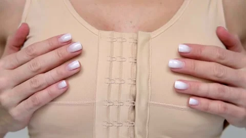 A woman demonstrating compression post-surgery bra in a medical office, plastic Video stock 342615077