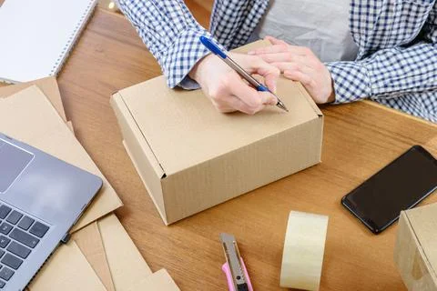Woman at the desk marks the e-commerce order packed in a cardboard box with a Stock Photos