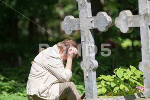 A woman in desperation sits at a grave in a cemetery Stock Photos