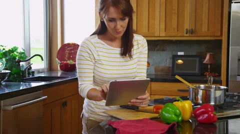 Woman with digital tablet in kitchen cooking Stock Footage
