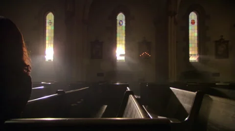 Woman in dimly lit church saying prayers with rosary Stock Footage