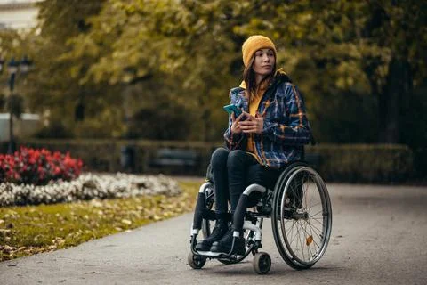 Woman with disability using a smartphone while out in the city park Stock Photos
