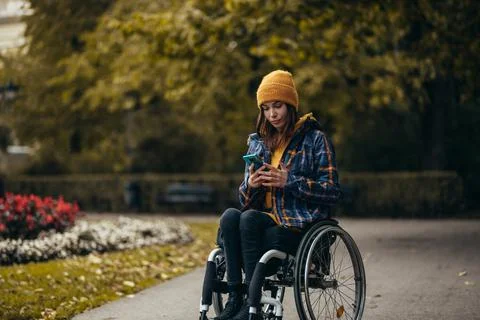 Woman with disability using a smartphone while out in the city park Stock Photos