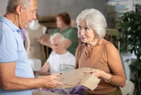 Woman discussing pattern with classmate during sewing course for older adults 库存照片