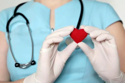 Woman doctor in medical mask holding red knitted heart in hands Stock Photos