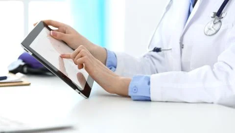 Woman doctor using tablet computer while sitting in hospital office closeup Stockfoto's
