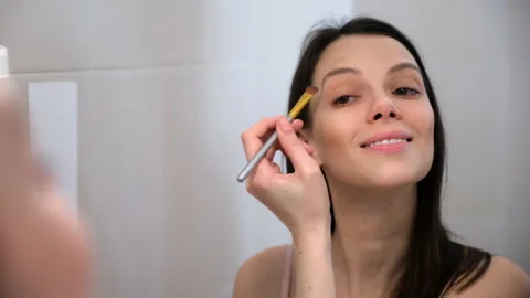 Woman does face contouring using concealer palette with brush looking at mirror. Stock Footage 234814862