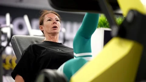 A woman does a leg press in a simulator, a tense face, an emphasis on effort   Stock Footage 313869207