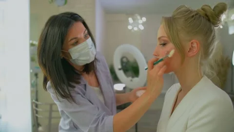 A woman does makeup in her Studio in a medical mask, Quarantine measures in a Stock Footage 136511230