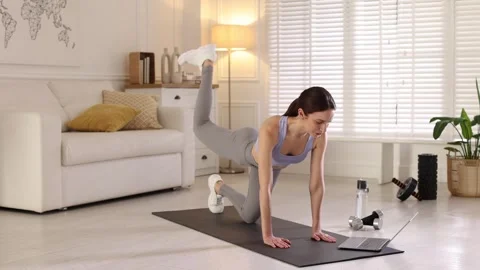 Woman doing exercise while watching video tutorial via laptop at home Vídeos de archivo 305597979