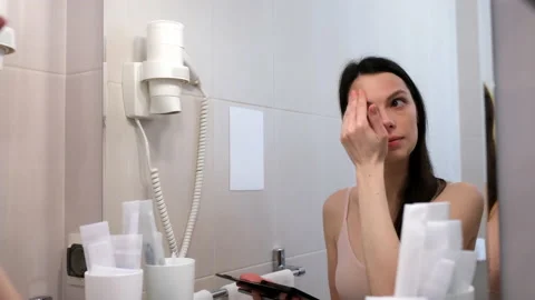 Woman is doing face contouring using concealer palette looking at mirror. Stock Footage 238734486