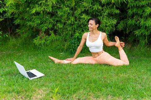 Woman doing Front splits with bind near laptop in park 写真素材