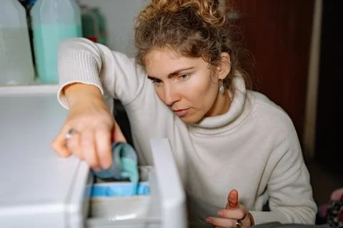 Woman doing laundry at home while pouring detergent into washing machine duri Stock Photos