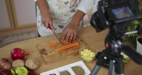 Woman doing live stream chops carrots while cooking, wide shoot 스톡 동영상 142252912