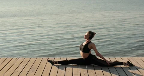 Woman is doing longitudinal split sitting on pier near river and tilting to leg. Stock Footage 138396604