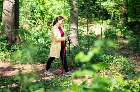 Woman doing Nordic walking alone in green forest, wearing sporty outfit, enjo Stock Photos