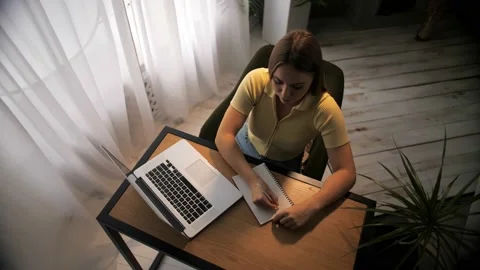 Woman doing online learning using note pad sitting at table in home interior Stock Footage 209828780