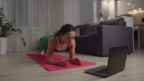 Woman doing plank exercise, watching video tutorial on laptop indoors Video stock 167352789