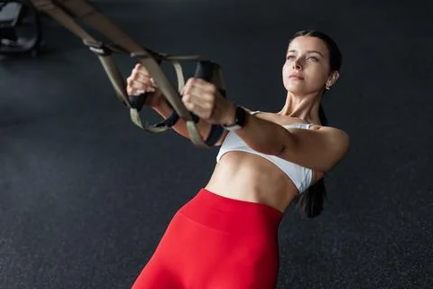 Woman doing pull ups training arms with trx fitness straps in the gym. Uppe.. Stock Photos