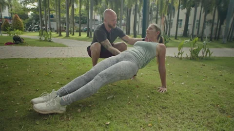 Woman Doing Reverse Plank with Help of Personal Trainer in Park Stock Footage 238827194