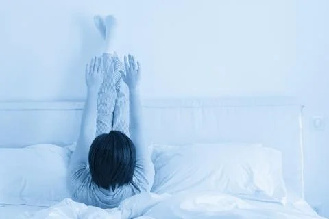 Woman doing some exercise lying in bed with legs high up Stock Photos