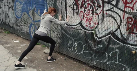 Woman doing stretching exercise leaning against graffiti wall Vídeo Stock 63374686
