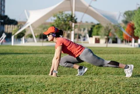 Woman doing stretching exercises while listening to music in a park Stock Photos