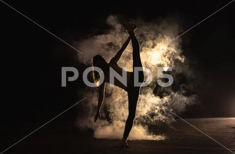 The woman doing vertical split in the smoke on the dark background Stock Photos