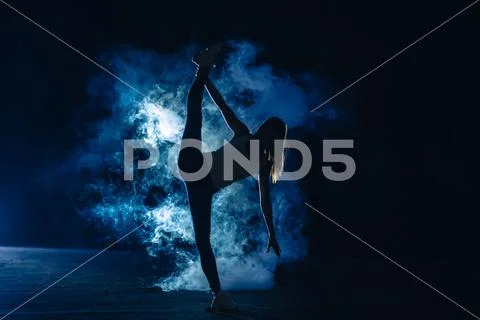 The woman doing vertical split in the smoke on the dark background Stock Photos