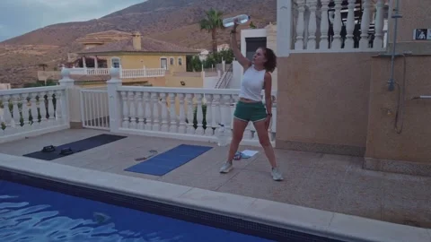 Woman Doing Windmill Core Exercise with Water Bottle Poolside on Terrace Stock Footage 345026002