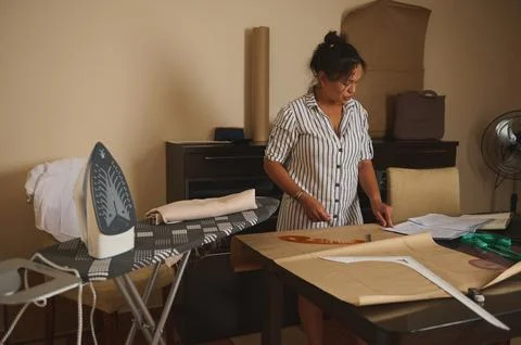 Woman drafting a sewing pattern and measuring fabric at home workspace with.. Stock Photos
