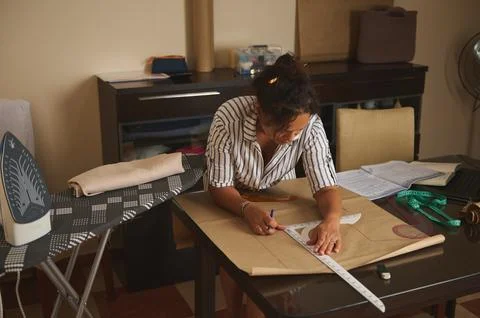 Woman drafting a sewing pattern on kraft paper at home table with measuring.. Stock Photos