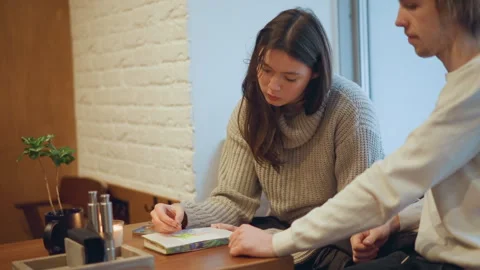 Woman drawing in cozy cafe while man sits beside her featuring notebook pen Stock Footage 346733567
