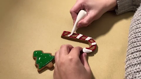 Woman draws pattern on gingerbread in shape of candy cane Stock Footage 289797109