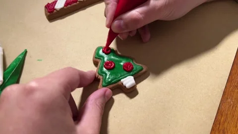 Woman draws red pattern on gingerbread cookie in shape of Christmas tree Stock Footage 287779902