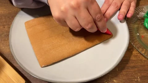 Woman draws red wave pattern on gingerbread house roof in plate on table Vídeos de archivo 340427925