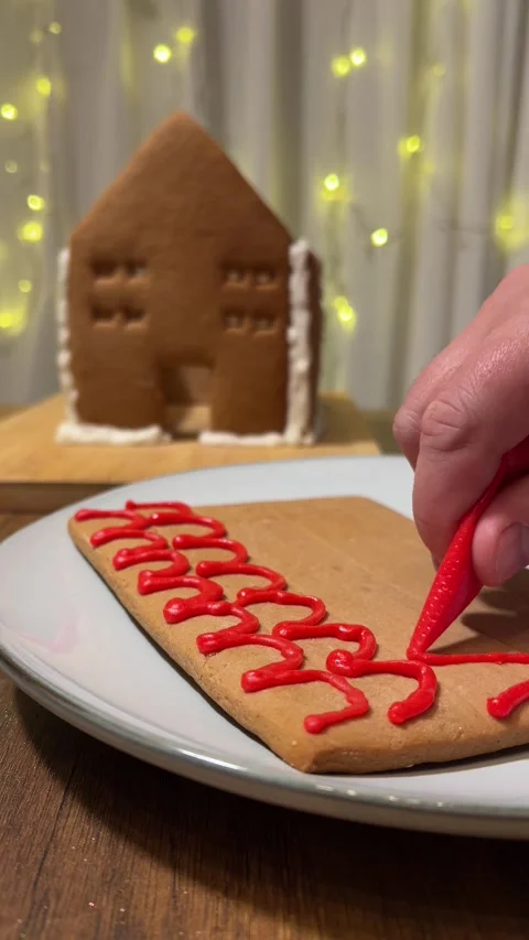Woman draws wavy pattern on gingerbread cookie in plate on table Stock Footage 299968259