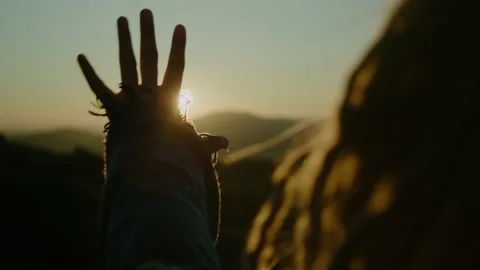 Woman with dreadlocks looking at sun through her fingers at sunset 스톡 동영상 148409530