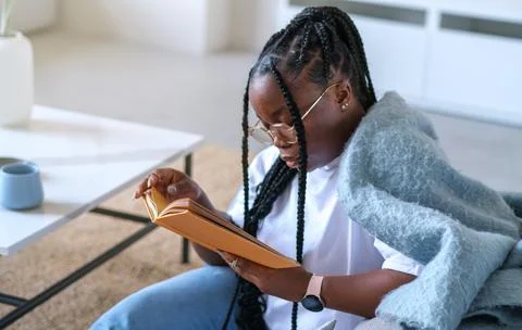 A woman with dreadlocks is reading a book while wrapped in a blanket Stock Photos