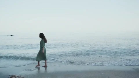 Woman in a dress walking along the seashore in the sunset while the blue hour Stock Footage