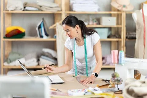 Woman dressmaker draws pattern using drawing on laptop Stock Photos