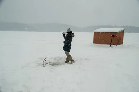 Woman Drinking from a Bottle While Ice Fishing Near a Hut in a Snowstorm Foto stock