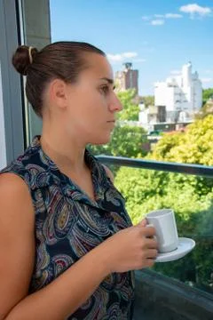 Woman drinking coffee and looking out the window during quarantine Stock Photos