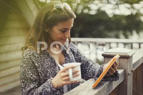 Woman drinking coffee and using digital tablet on balcony Stock Photos