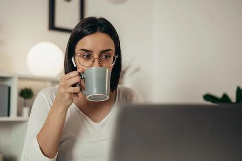 Woman drinking coffee and using a laptop while working from home Stock Photos