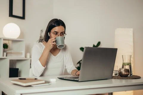 Woman drinking coffee and using a laptop while working from home Stock Photos